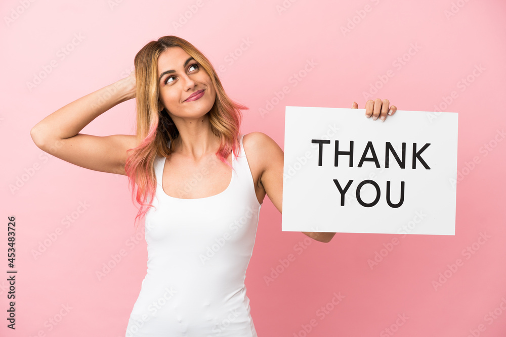 Young woman over isolated pink background holding a placard with text THANK YOU and thinking Young woman over isolated pink background holding a placard with text THANK YOU and thinking