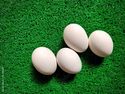 Four raw white eggs in zigzag manner isolated on green background photo