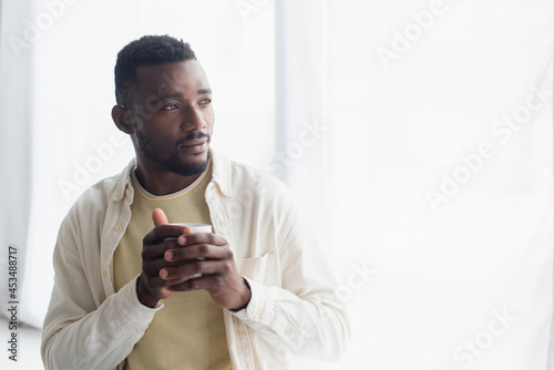 pensive african american man holding cup of coffee in morning © LIGHTFIELD STUDIOS