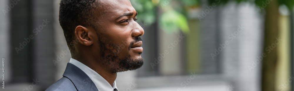 Obraz premium side view of bearded african american businessman in suit looking away, banner