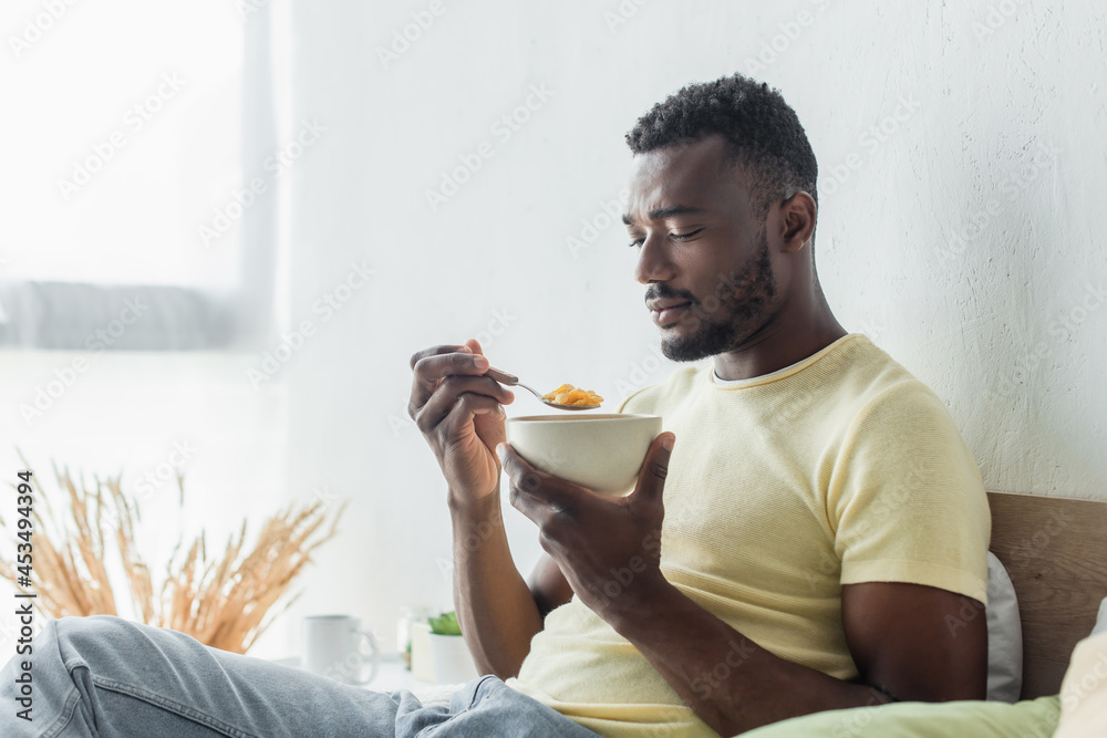 young african american man looking at corn flakes in bowl