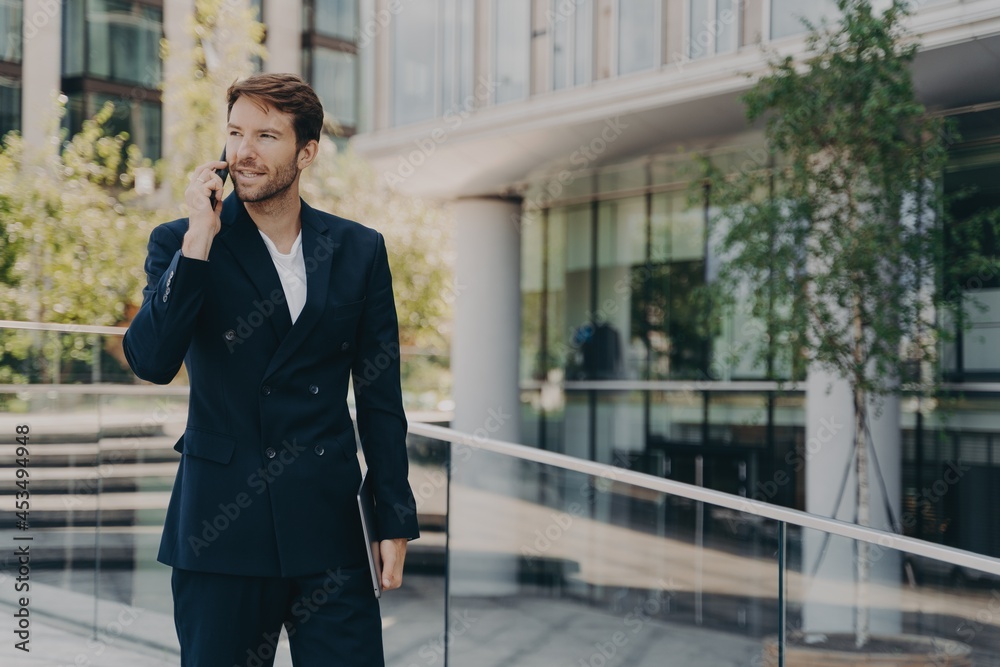Young man office worker in suit talking on mobile phone while walking outside of business center Young man office worker in suit talking on mobile phone while walking outside of business center