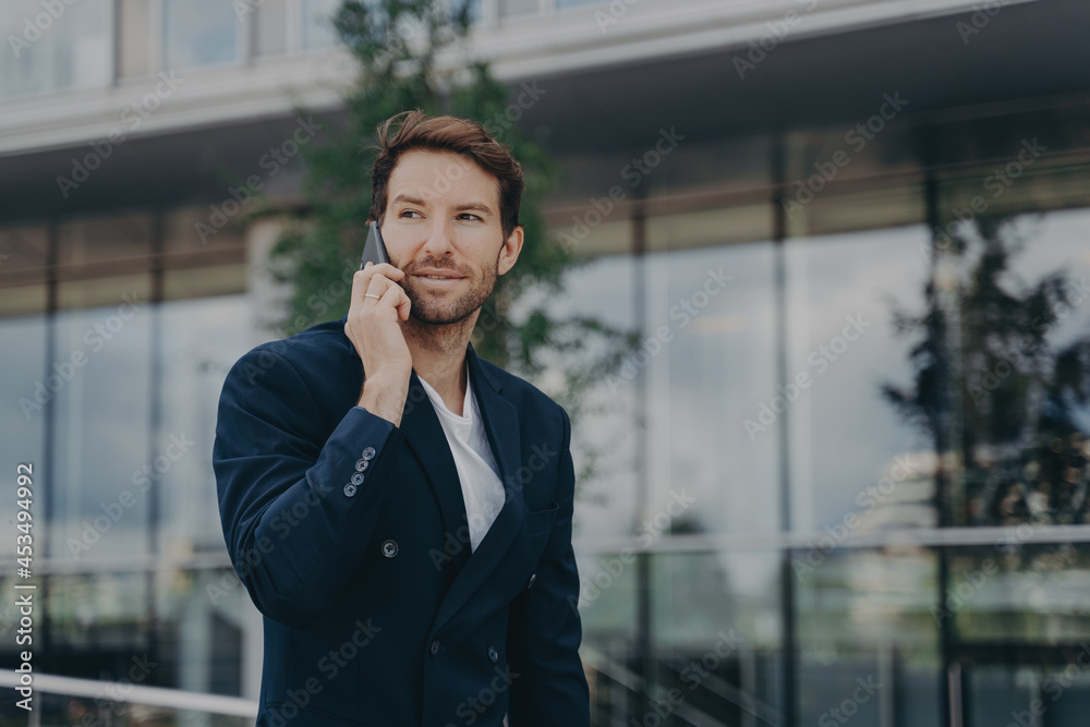 Male entrepreneur talks via phone solves urgent problems poses near business center Male entrepreneur talks via phone solves urgent problems poses near business center