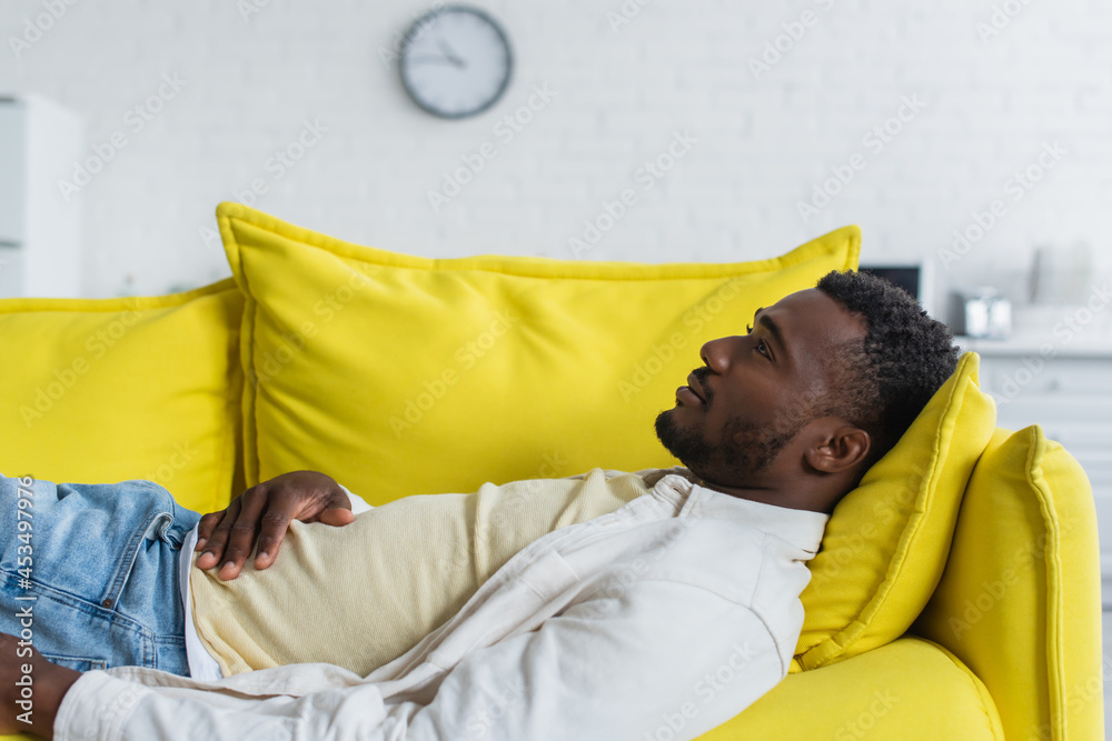 young african american man lying on yellow couch young african american man lying on yellow couch