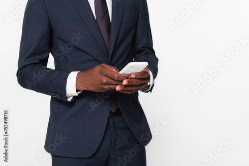 cropped view of african american businessman in suit messaging on smartphone isolated on grey