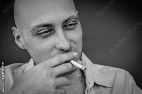 black and white portrait of a young bald man smoking a cigarette while relaxing and looking in front of him