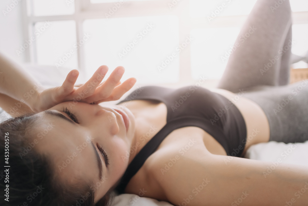 Asian woman in sport wears is resting after workout in her bedroom. Asian woman in sport wears is resting after workout in her bedroom.