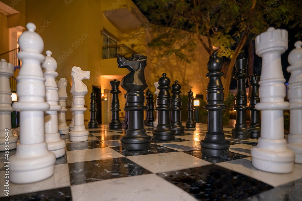 Big plastic chess pieces at hotel yard in evening. Chessboard game, strategy, ideas. Chess knight in center position