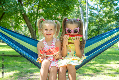 Two cheerful little girls eating watermelon while sitting on a hammock