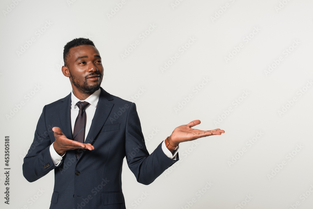 smiling african american businessman in suit pointing with hands isolated on grey smiling african american businessman in suit pointing with hands isolated on grey