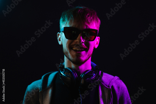 Neon portrait of a bearded man wearing headphones on the neck, wearing parka and sunglasses. Hacker portrait