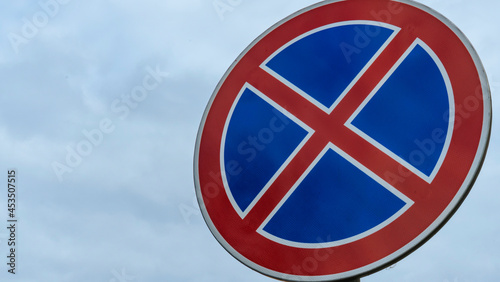 Round road sign with a red cross on a blue background. A sign means a parking prohibition. Dramatic sky background. Space for text.