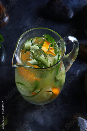 Homemade cold lemonade based on cucumber, mint and orange. Fresh fruit in a misted glass jar. Pieces of ice. Black background.Vertical photo. Summer menu.Top view.