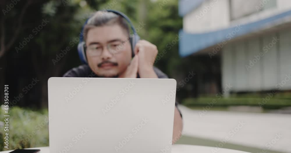Asian Obese man wearing glasses, headphone to video call with laptop meeting outside. webinar with colleagues. using video conference app video call virtual communication. entertainment online Asian Obese man wearing glasses, headphone to video call with laptop meeting outside. webinar with colleagues. using video conference app video call virtual communication. entertainment online