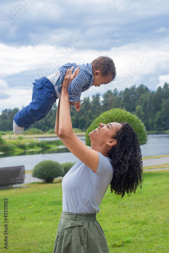 Young beautiful dark-skinned mother holds her baby up