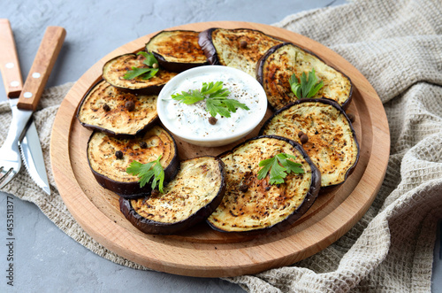 Grilled eggplant with spices, herbs and sauce on a wooden plate on a gray background. A healthy snack. Selective focus