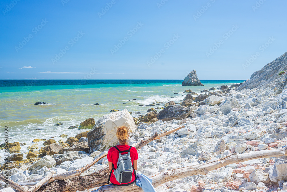 Woman relaxing on italian beach. Uneven Conero coast line, pebble beach, turquoise water real people, rear view, sunny day, vacation in Italy