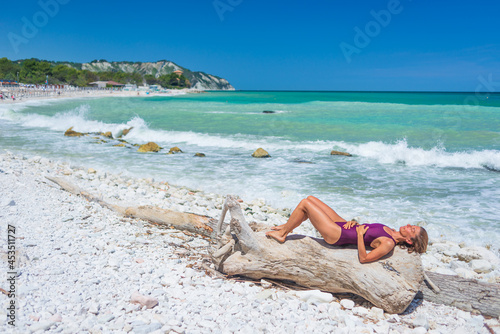 Fototapeta Naklejka Na Ścianę i Meble -  Woman relaxing on italian beach. Uneven Conero coast line, pebble beach, turquoise water real people, side view, sunny day, vacation in Italy