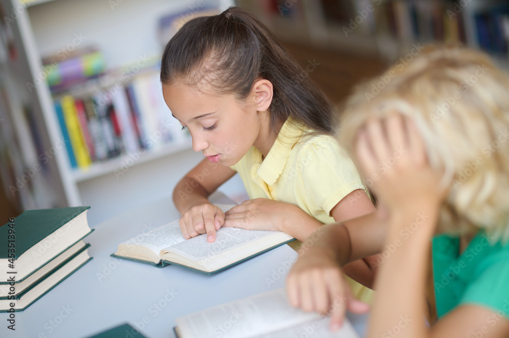 Two focused schoolchildren studying together at the library Two focused schoolchildren studying together at the library