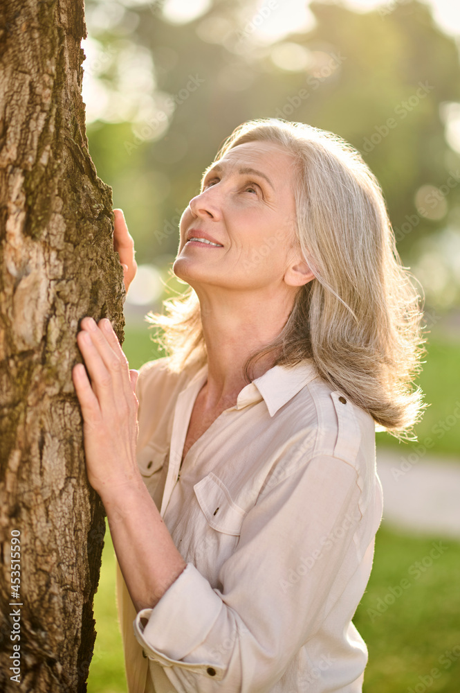 Woman touching tree with her palms looking up Woman touching tree with her palms looking up