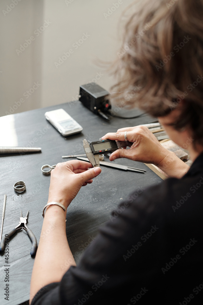 Over shoulder view of female jeweler measuring ring width using caliper in workshop
