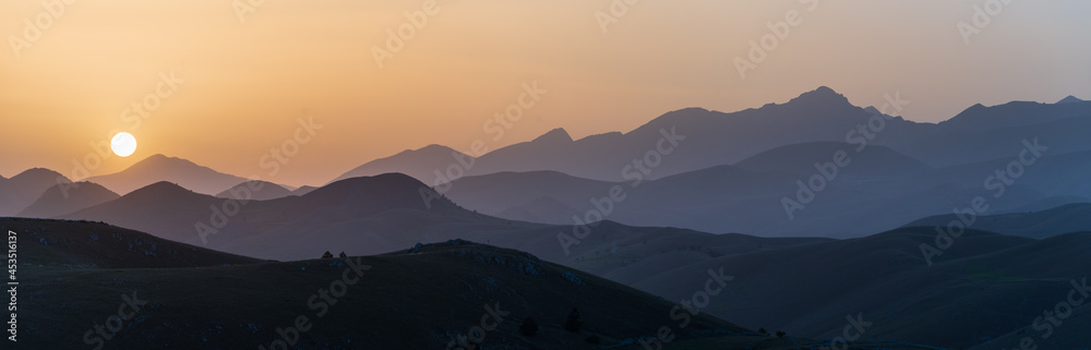 Sunset view point on rocky mountains silhouette. Campo Imperatore, Gran Sasso, Apennines, Italy. Clear sky sun burst on dramatic mountain ridge.