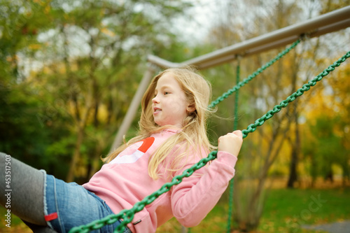 Pretty young girl having fun on a playground in beautiful autumn park. Cute preteen child playing outdoors in late autumn. Outdoor activities for kids.