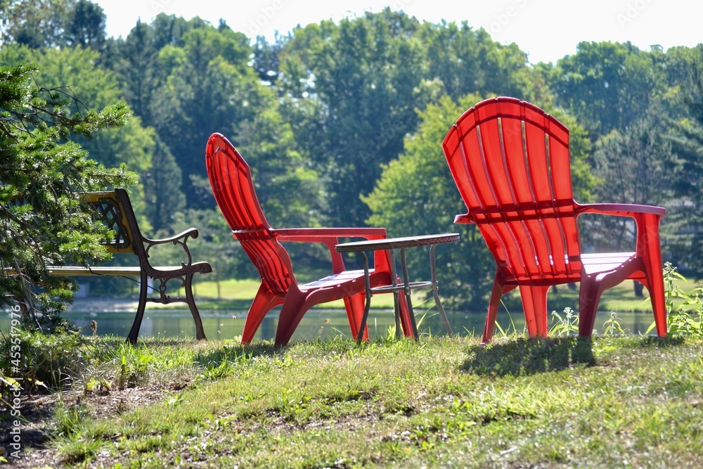 Red Adirondack chairs and bench on the edge of a lake a relaxing tranquil scene.