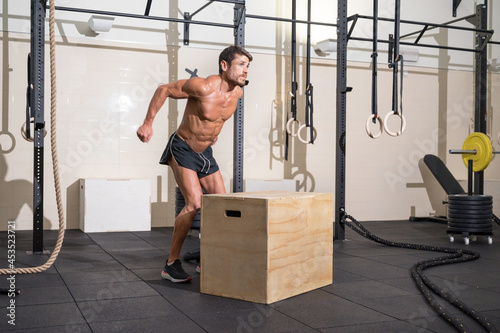 Muscular male athlete is practicing jumping on a wooden box in modern health club. Functional training. High quality photo