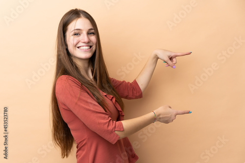 Young caucasian woman isolated on beige background pointing finger to the side and presenting a product