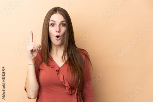 Young caucasian woman isolated on beige background intending to realizes the solution while lifting a finger up