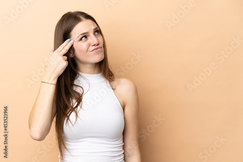 Young caucasian woman isolated on beige background with problems making suicide gesture