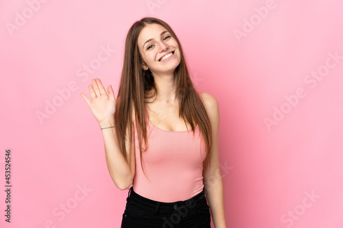 Young caucasian woman isolated on pink background saluting with hand with happy expression