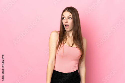 Young caucasian woman isolated on pink background doing surprise gesture while looking to the side