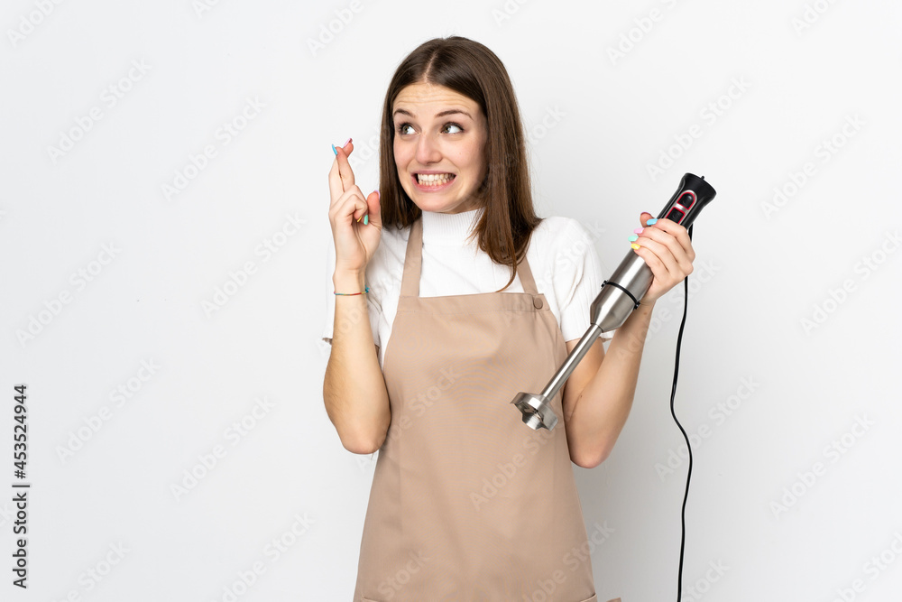 Young woman using hand blender isolated on white background with fingers crossing
