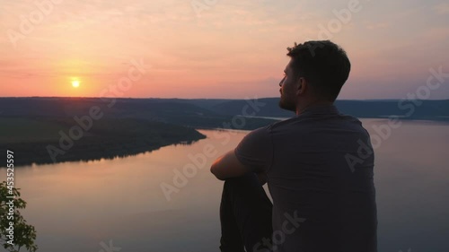 The young man sitting on rocky mountain above the beautiful river. slow motion