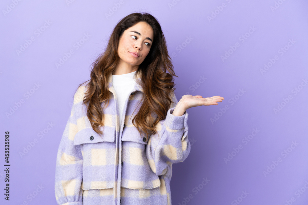 Woman over isolated purple background holding copyspace with doubts Woman over isolated purple background holding copyspace with doubts