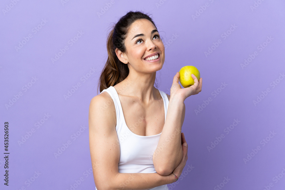 Woman over isolated purple background with an apple and happy Woman over isolated purple background with an apple and happy
