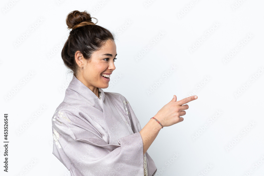Woman wearing kimono over isolated background pointing finger to the side and presenting a product Woman wearing kimono over isolated background pointing finger to the side and presenting a product