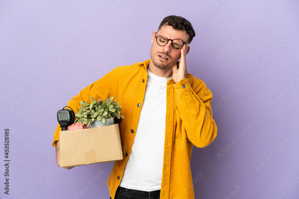 Young caucasian man making a move while picking up a box full of things isolated on purple background with headache Young caucasian man making a move while picking up a box full of things isolated on purple background with headache