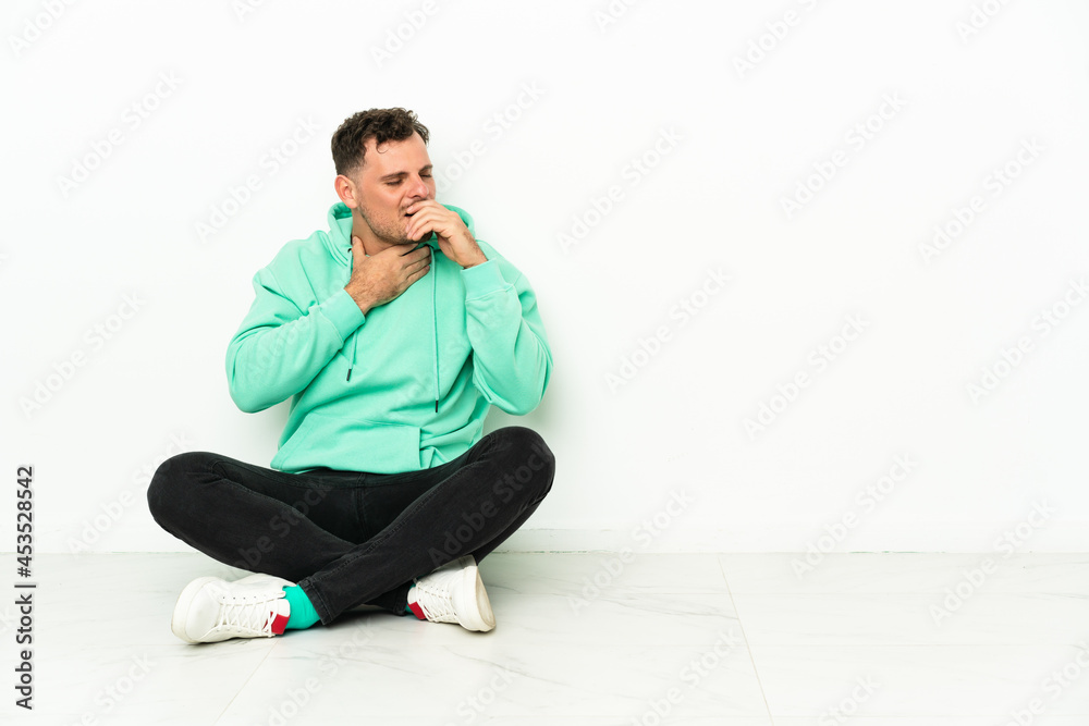 Young handsome caucasian man sitting on the floor is suffering with cough and feeling bad Young handsome caucasian man sitting on the floor is suffering with cough and feeling bad