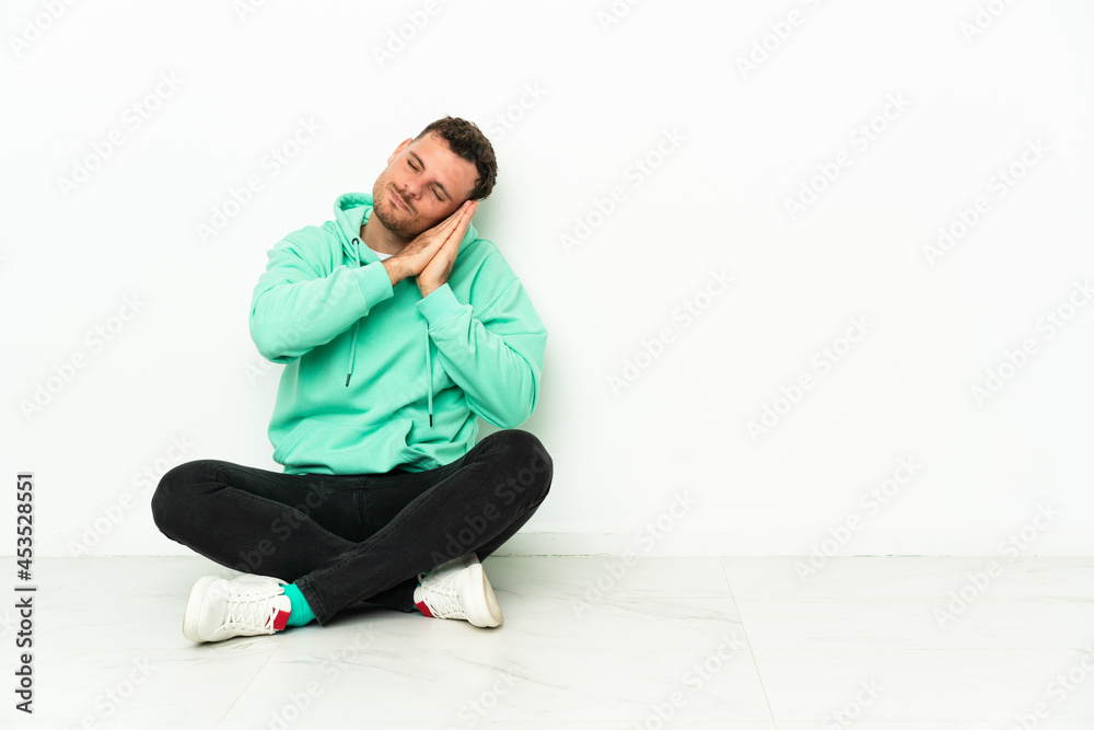 Young handsome caucasian man sitting on the floor making sleep gesture in dorable expression