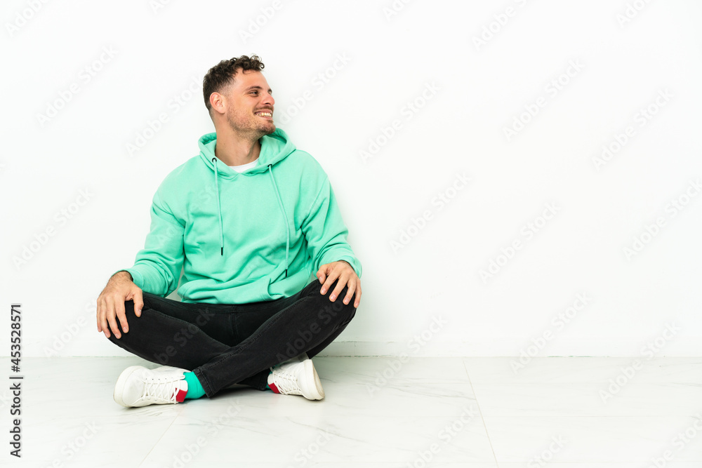Young handsome caucasian man sitting on the floor laughing in lateral position Young handsome caucasian man sitting on the floor laughing in lateral position