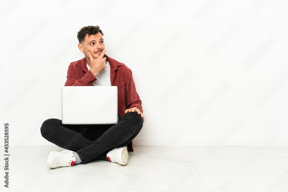 Young handsome caucasian man sit-in on the floor with laptop having doubts and with confuse face expression Young handsome caucasian man sit-in on the floor with laptop having doubts and with confuse face expression