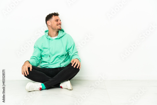 Young handsome caucasian man sitting on the floor laughing in lateral position