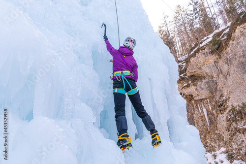 Female ice climber climbing up the side of an icy slope with bumps, ridges, and icicles