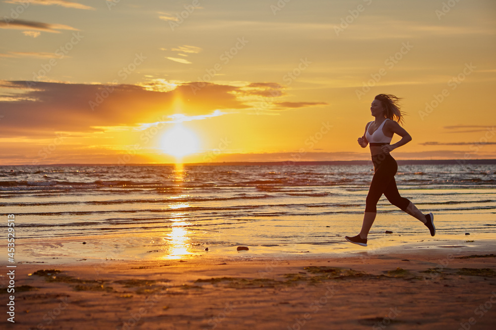 Slim woman runs on shore during sunset.
