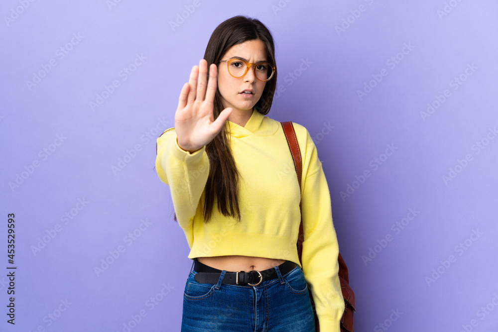 Teenager Brazilian student girl over isolated purple background making stop gesture with her hand Teenager Brazilian student girl over isolated purple background making stop gesture with her hand