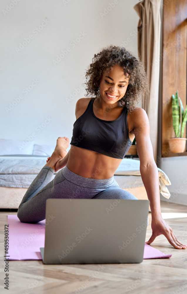 Φωτογραφία Young happy healthy African American mixed race girl wears sportswear doing fitness exercise workout remotely watching online class tutorial on laptop pc at home sit on mat feeling harmony