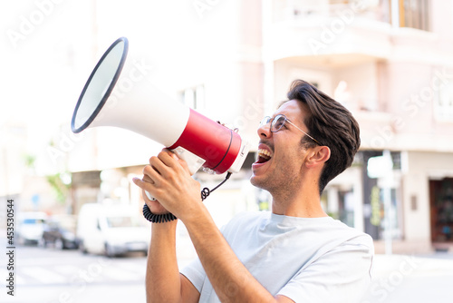 Photos Young caucasian man at outdoors shouting through a megaphone to announce somethi